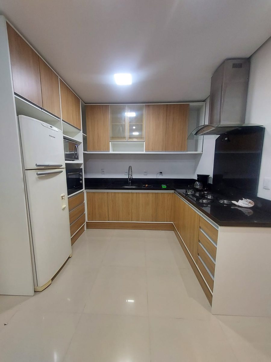 Cozinha em L com armários amadeirados, torre de forno e coifa