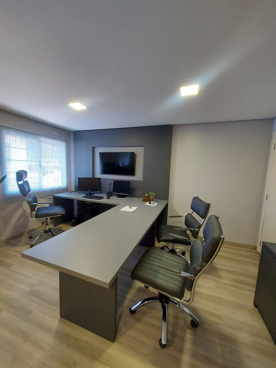Escritório com mesa em U cinza, painel de TV e cadeiras